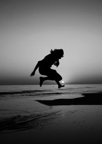 Silhouette man jumping on beach against clear sky