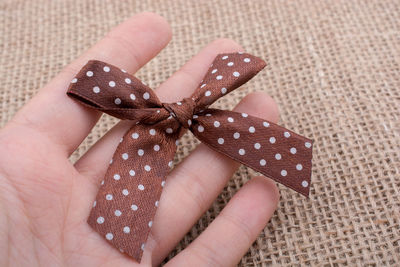 Close-up of hand holding brown tied bow at table