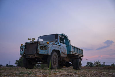 Abandoned car on field against sky during sunset