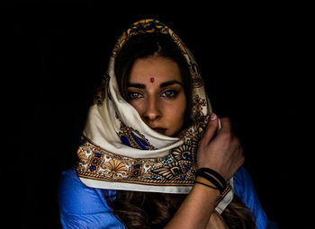 Portrait of young woman wearing headscarf over black background