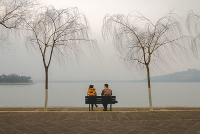Rear view of couple sitting on lake against sky