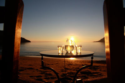 Drinking glasses and jug on table at beach during sunset