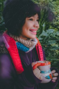 Close-up of thoughtful girl smiling while having drink in cup against plants