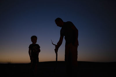 Silhouette of man and child standing on land against sky during sunset
