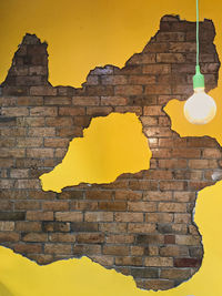 Close-up of illuminated light bulb against yellow wall