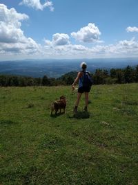 Rear view of man with dog standing on grassy field