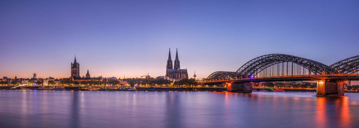 Illuminated bridge over river against sky in city at dusk