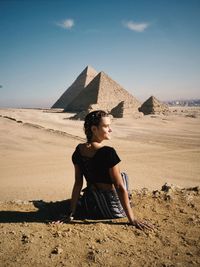 Young woman sitting on sand at desert against sky