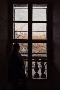 Silhouette mid adult woman looking through window while standing at home