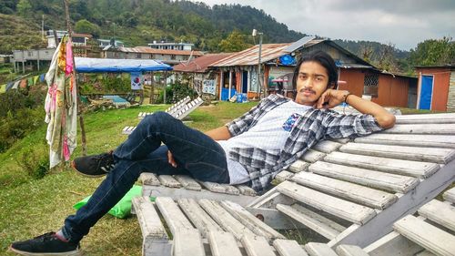 Portrait of young man leaning on chair against houses in town