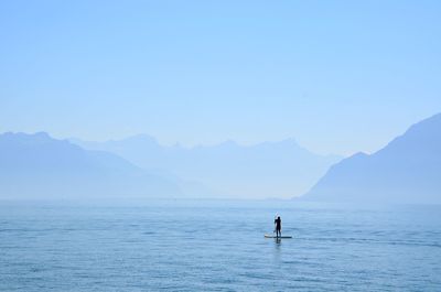 Silhouette person paddleboarding in sea against clear sky