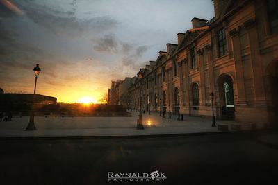 Street by buildings against sky during sunset