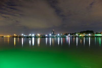 Illuminated city by sea against sky at night