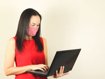 Young woman using mobile phone against wall