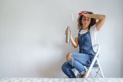 Young woman sitting against wall at home