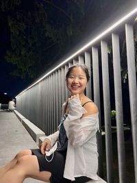 Smiling woman sitting by railing at night