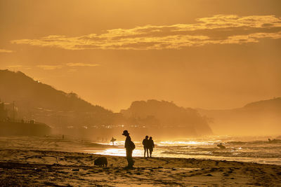 Silhouette people on beach against sky during sunrise