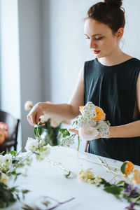 High angle view of woman arranging flowers in vase at table