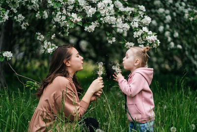 Mother and daughter with dandelions blooming apple trees