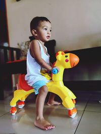 Side view of baby boy playing on horse toy at home