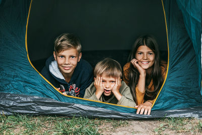 Smiling children lie together in a tent at a camping site. family time, family vacation