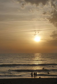 Silhouette people on beach against sky during sunset