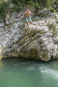 Full length of shirtless man on rock diving in sea