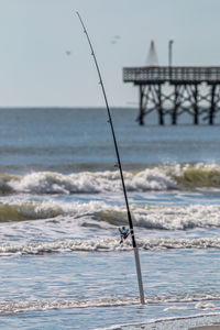 Scenic view of a fishing pole waits along the ocean surf coast with a pier in background clear day