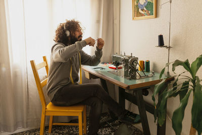 Bearded man stitching face mask sitting at home