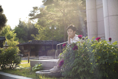 Woman sitting by plants against trees