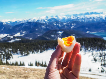 Close-up of hand having boiled egg against snowcapped mountains