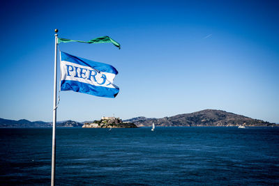Information sign by sea against clear blue sky