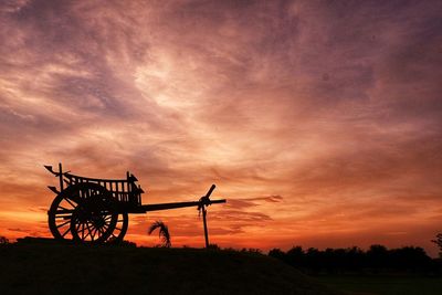 Silhouette of ferris wheel on field against dramatic sky