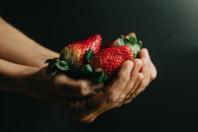 Cropped image of hand holding strawberry against black background