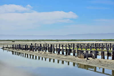 Wooden posts in lake against sky