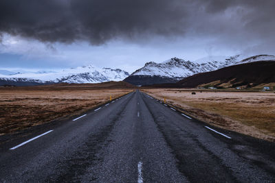 Empty road leading towards snowcapped mountains against sky