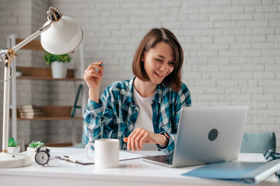 Young woman using mobile phone while sitting on table