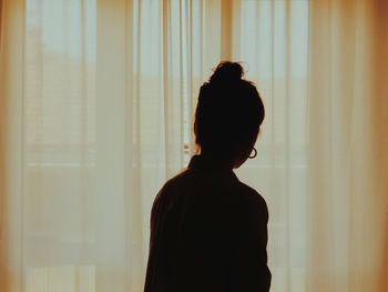 Rear view of silhouette woman standing against window at home