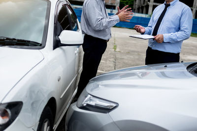 Midsection of salesman and customer standing by cars