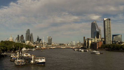 Boats in river by buildings in city against sky