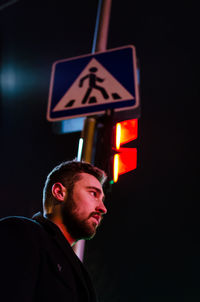Low angle view of man standing by road sign against sky at night