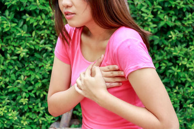 Midsection of young woman suffering from chest pain against plants