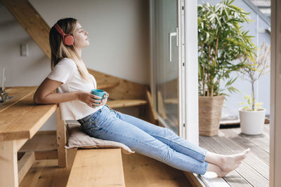 Young woman relaxing at home with a cup of tea, listening music