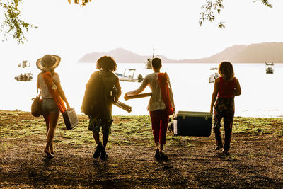 Back view full body of young friends carrying food and supplies for summer picnic on beach of costa rica