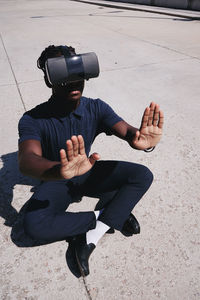 High angle view of teenager gesturing while using virtual reality on road during sunny day