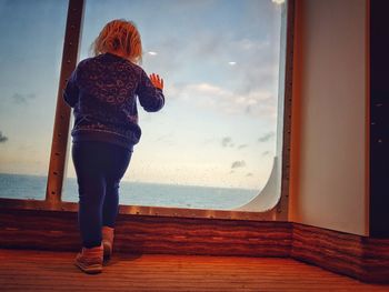 Rear view of woman standing by sea against sky