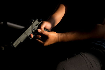 Midsection of man holding handgun while sitting on chair in room