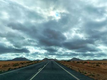 Empty road along landscape against cloudy sky