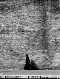 Woman walking on sidewalk against brick wall