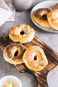 Bagels with poppy seeds and sesame on the board and butter in a bowl on the table.